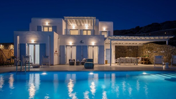 A modern villa with a swimming pool, outdoor seating, and a stone wall. - Chrysanthemo Villas (Mykonos)