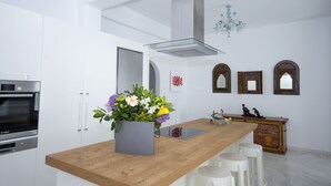 A modern kitchen with white cabinetry, a Bosch oven, a wooden countertop, and a vase of flowers. - Chrysanthemo Villas (Mykonos)