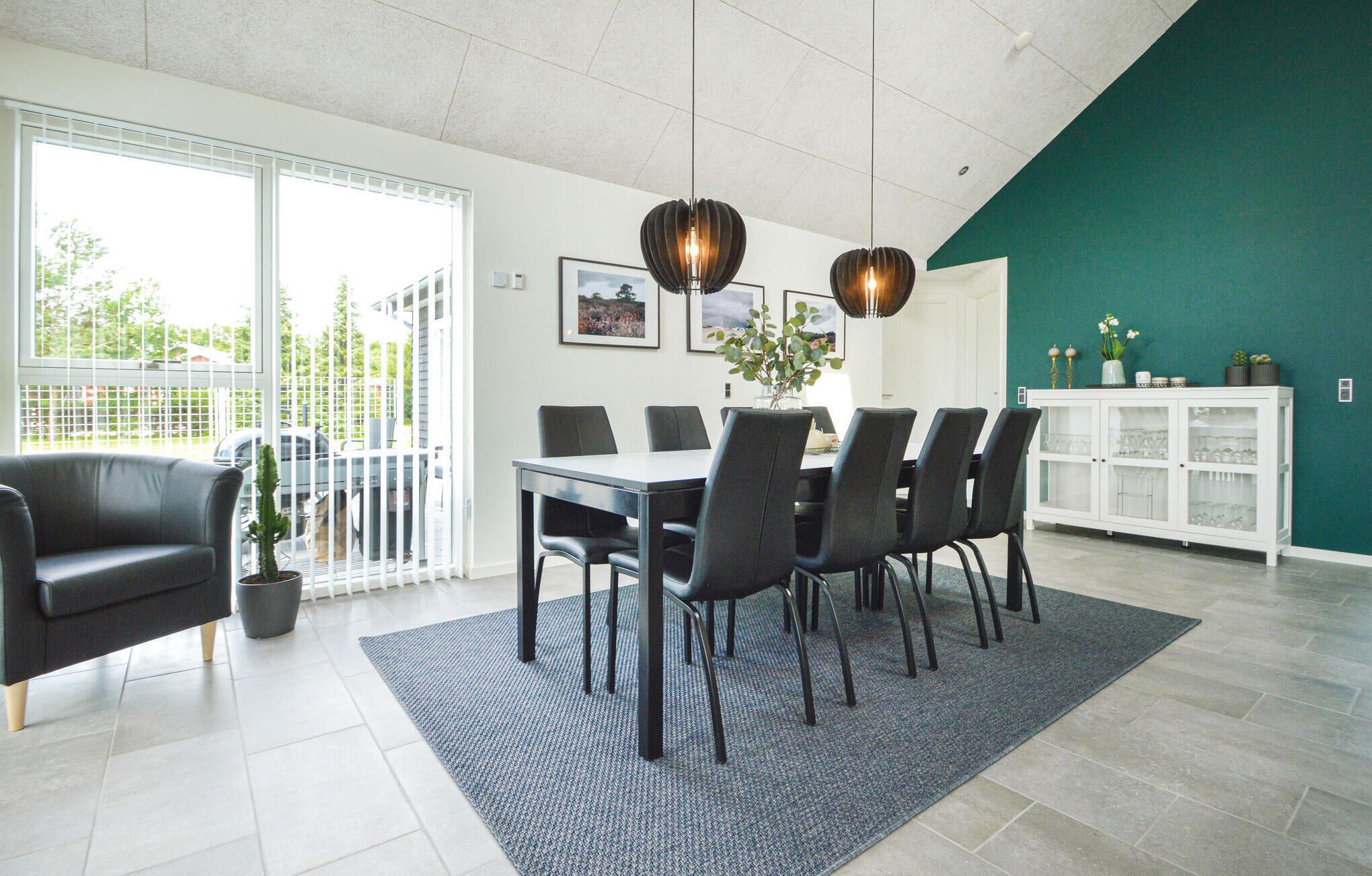 Ein moderner Essbereich mit einem weißen Tisch, schwarzen Stühlen, einem schwarzen Sofa und einer Wand in Türkis.