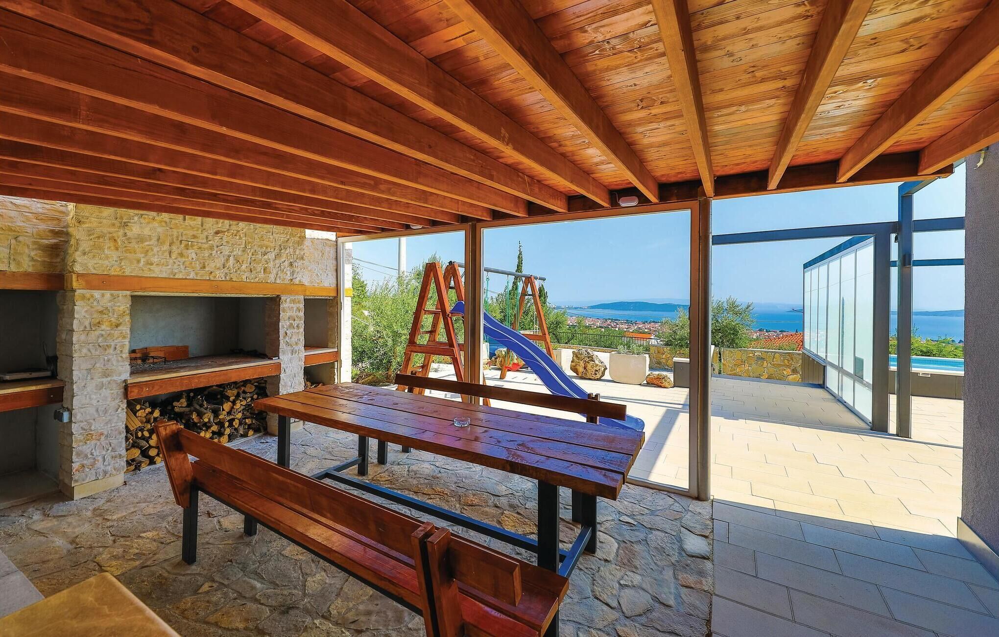 A covered outdoor area with a wooden bench, stone walls, and a view of a playground and sea.