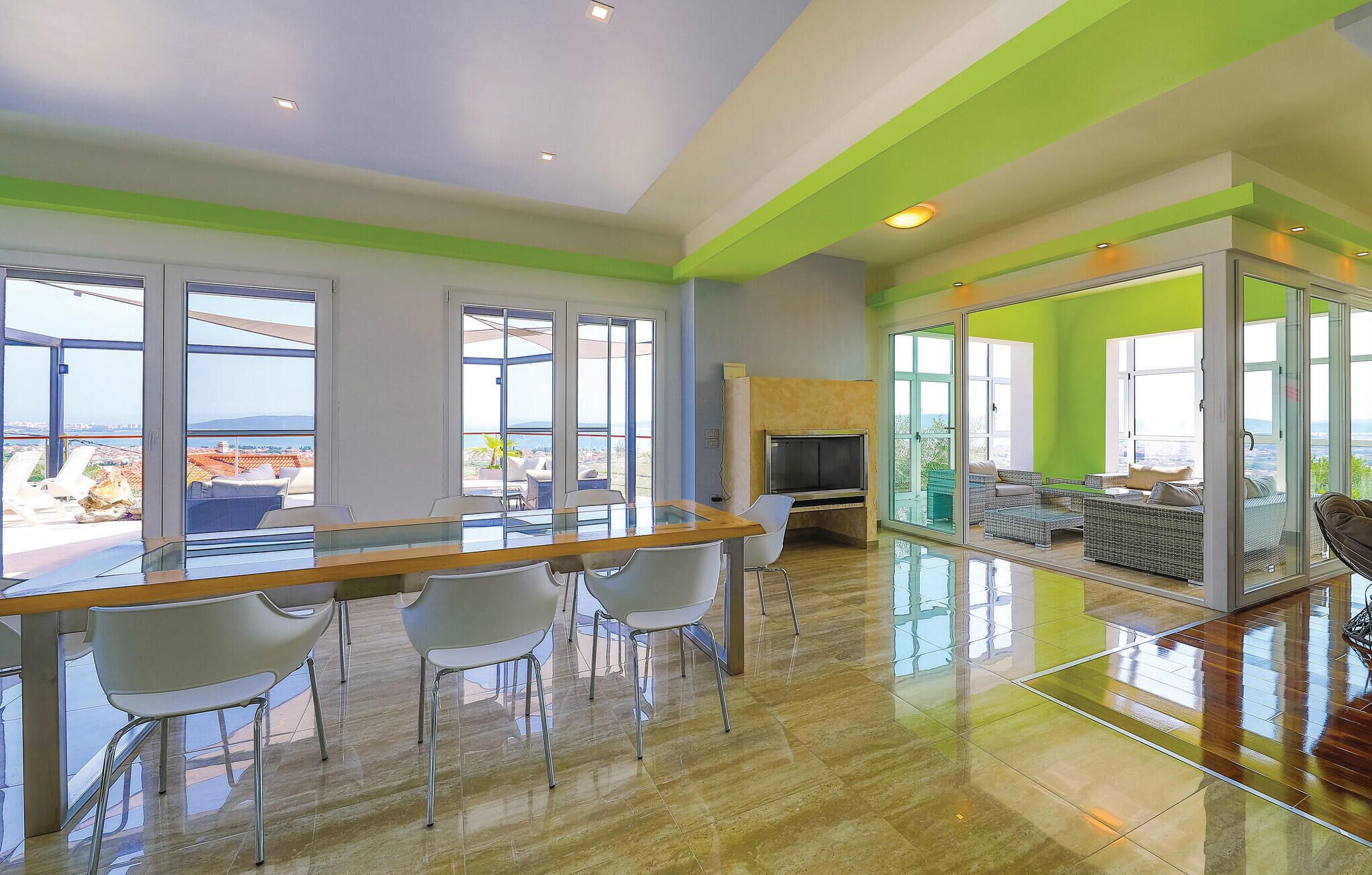 A spacious living area with a glass partition, a wooden dining table with chairs, and a television.