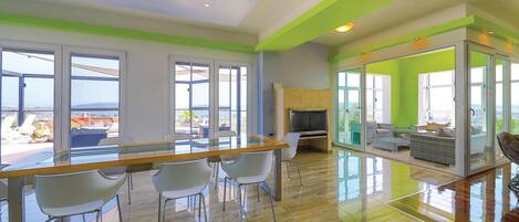 A spacious living area with a glass partition, a wooden dining table with chairs, and a television.
