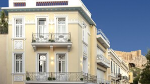 A hotel with a balcony, a shop on the ground floor, and a view of a mountain in the background. - Plaka Arch Suites (Athens)