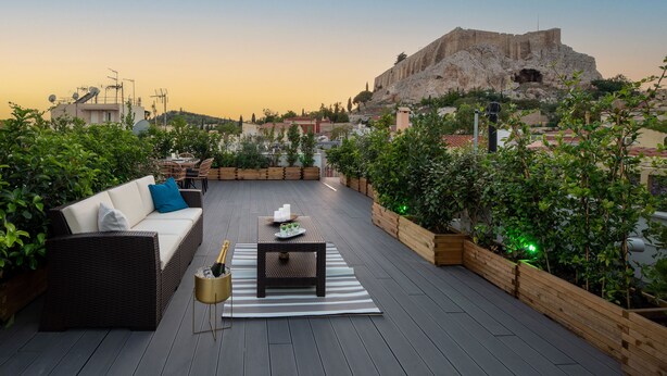 A rooftop terrace with a wicker sofa, a small table, and a bottle of champagne. - Plaka Arch Suites (Athens)