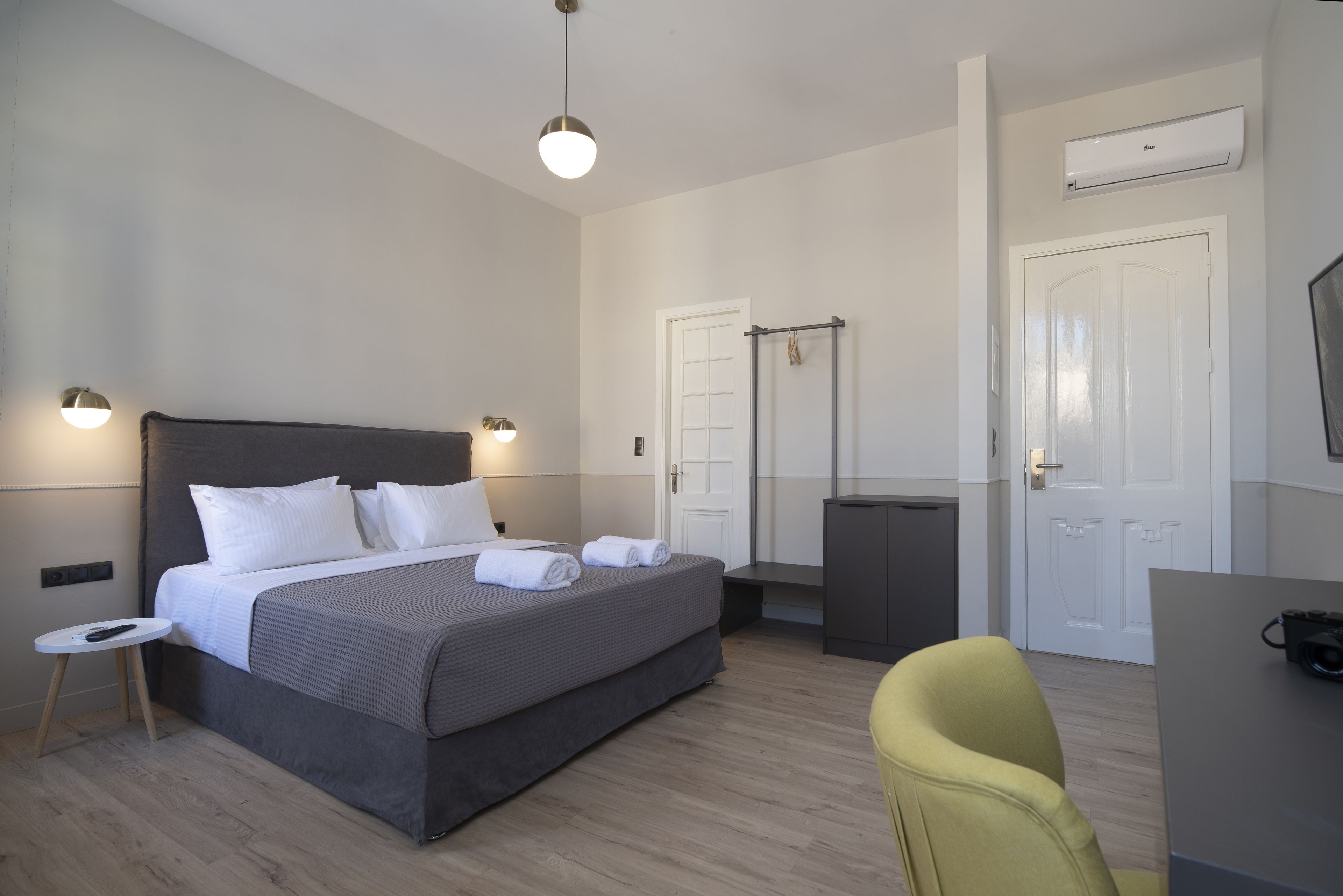 A modern hotel room with a large bed, bedside tables, a desk, and an air conditioning unit.