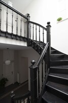 Escadaria curva com balaústres de madeira escura e corrimão preto, que leva a um andar superior.