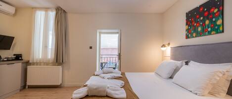 Habitación de hotel con cama, mesita de noche, radiador, ventana con cortinas, un cuadro en la pared y vistas al balcón exterior.