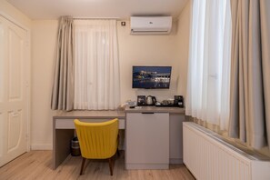 A compact hotel room with a kitchenette, a flat-screen TV, and a yellow chair.