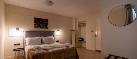 Un dormitorio con cama, lámparas de noche, un cuadro, un espejo y un banco de madera.