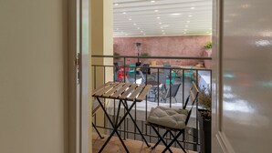 A balcony with a folding table and chairs, a cushioned bench, and a view of the interior space with a ceiling light fixture. - Plaka Arch Suites (Athens)
