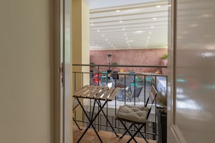 A balcony with a folding table and chairs, a cushioned bench, and a view of the interior space with a ceiling light fixture.