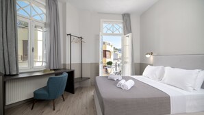 A hotel room with a bed, a desk, a chair, a radiator, and a view of the outside. - Plaka Arch Suites (Athens)