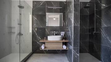 A modern bathroom with a glass-enclosed shower, a wooden vanity with a white sink, and marble walls.