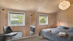 Un dormitorio con paredes de madera, una cama con ropa de cama gris, una silla y una mesita de noche con una lámpara.