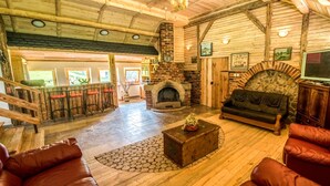 A spacious log cabin interior with a fireplace, leather seating, and a staircase leading to an upper level. - Zloty Potok Resort (Lesna)