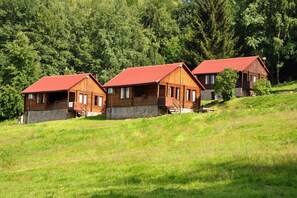 Three wooden cabins with red roofs on a grassy hillside, surrounded by dense forest. - Zloty Potok Resort (Lesna)