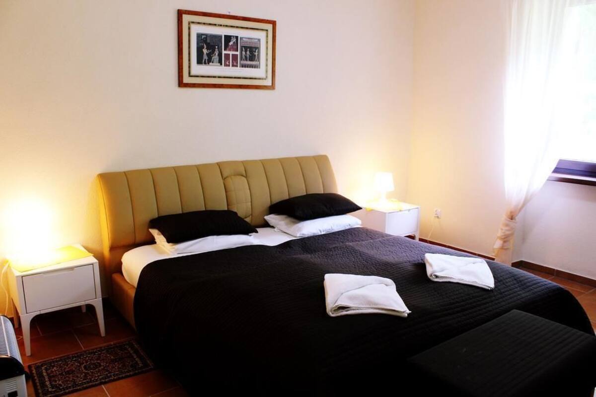 A neatly made bed with a headboard, two bedside lamps, and a framed picture on the wall.