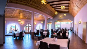 A spacious dining area with multiple tables and chairs, wooden ceiling beams, and natural light from large windows. - Zloty Potok Resort (Lesna)