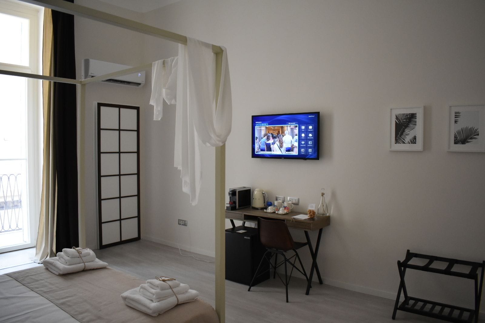 A hotel room with a bed, a desk with a chair, a television, and artwork on the wall.