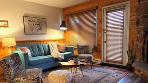 Een gezellige woonkamer met een blauwe bank, gestreept stoelen, een klein rond tafeltje en een decoratief vloerkleed.