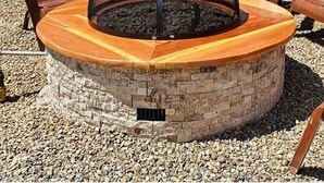 Een ronde vuurkuip van steen met een glazen deksel, omringd door Adirondack-stoelen.