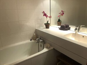 A bathroom with a white bathtub, a sink, and two potted orchids on the counter.