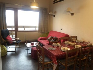 A dining area with a table set for four, a red sofa, a chair, and a window with curtains.