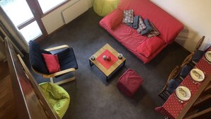 A cozy living room with a red sofa, a blue armchair, a wooden coffee table, and a dining area with a red tablecloth. - Marches 25 - 3 room duplex apartment, overlooking the slopes (LES AVANCHERS VALMOREL)