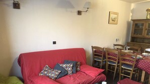 A red sofa with colorful pillows, a wooden table with a red placemat, and a dining area with wooden chairs and a table set for four. - Marches 25 - 3 room duplex apartment, overlooking the slopes (LES AVANCHERS VALMOREL)