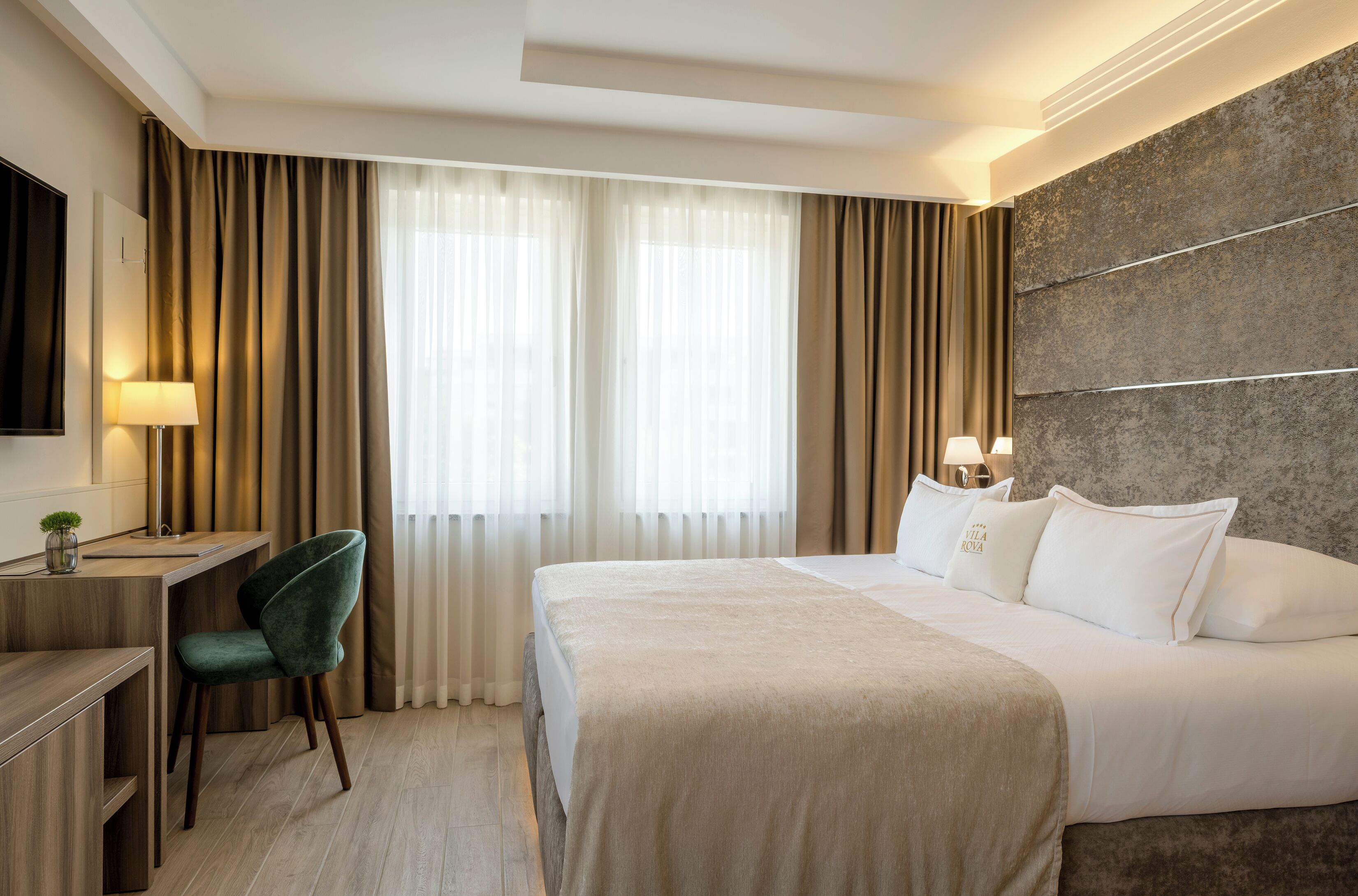A hotel room with a bed, desk, chair, and curtains.