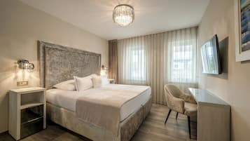Habitación de hotel con una cama grande, mesitas de noche, un escritorio, una silla, un televisor y un candelabro.