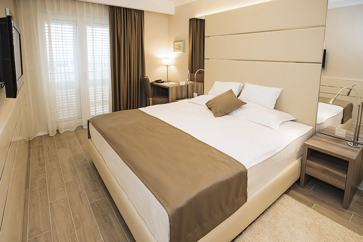 Een hotelkamer met een groot bed, een bureau, een stoel, een televisie en een spiegel in de badkamer.