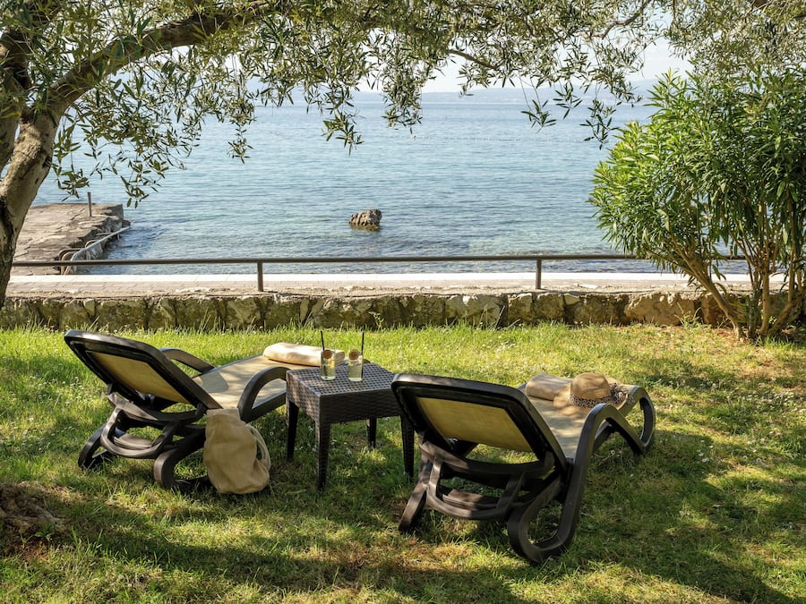 Un espace extérieur aménagé avec des tables et des chaises, situé en bord de mer, offrant une vue sur l’océan et bordé d’un mur en pierre.