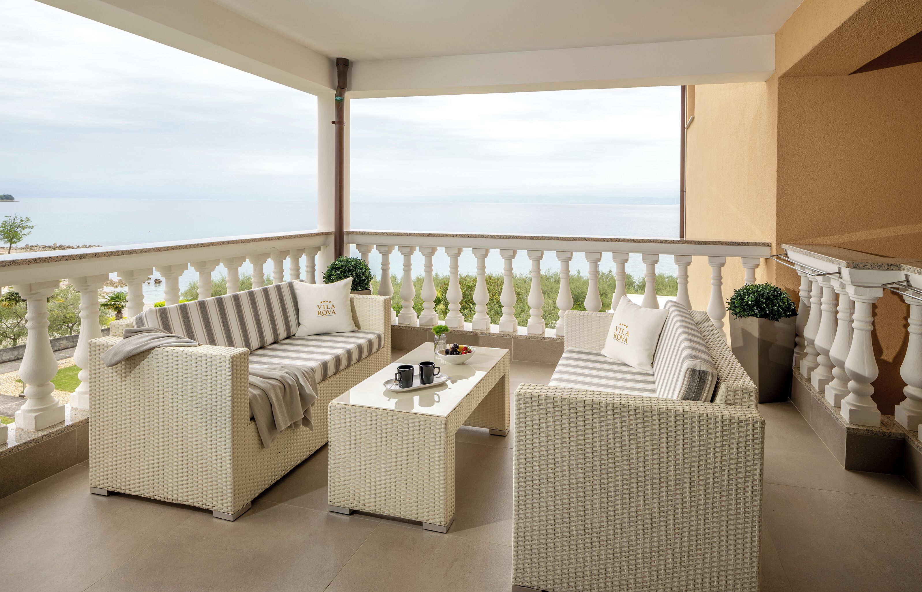 A balcony with wicker furniture, a coffee table, and a view of the sea.