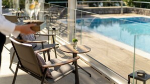 Un espace aménagé au bord de la piscine, avec des chaises et des tables, une rambarde en verre et une vue sur la piscine.