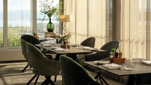 Un coin repas avec une table dressée pour quatre personnes, des chaises, un vase avec des plantes, une lampe et une vue sur l’extérieur.