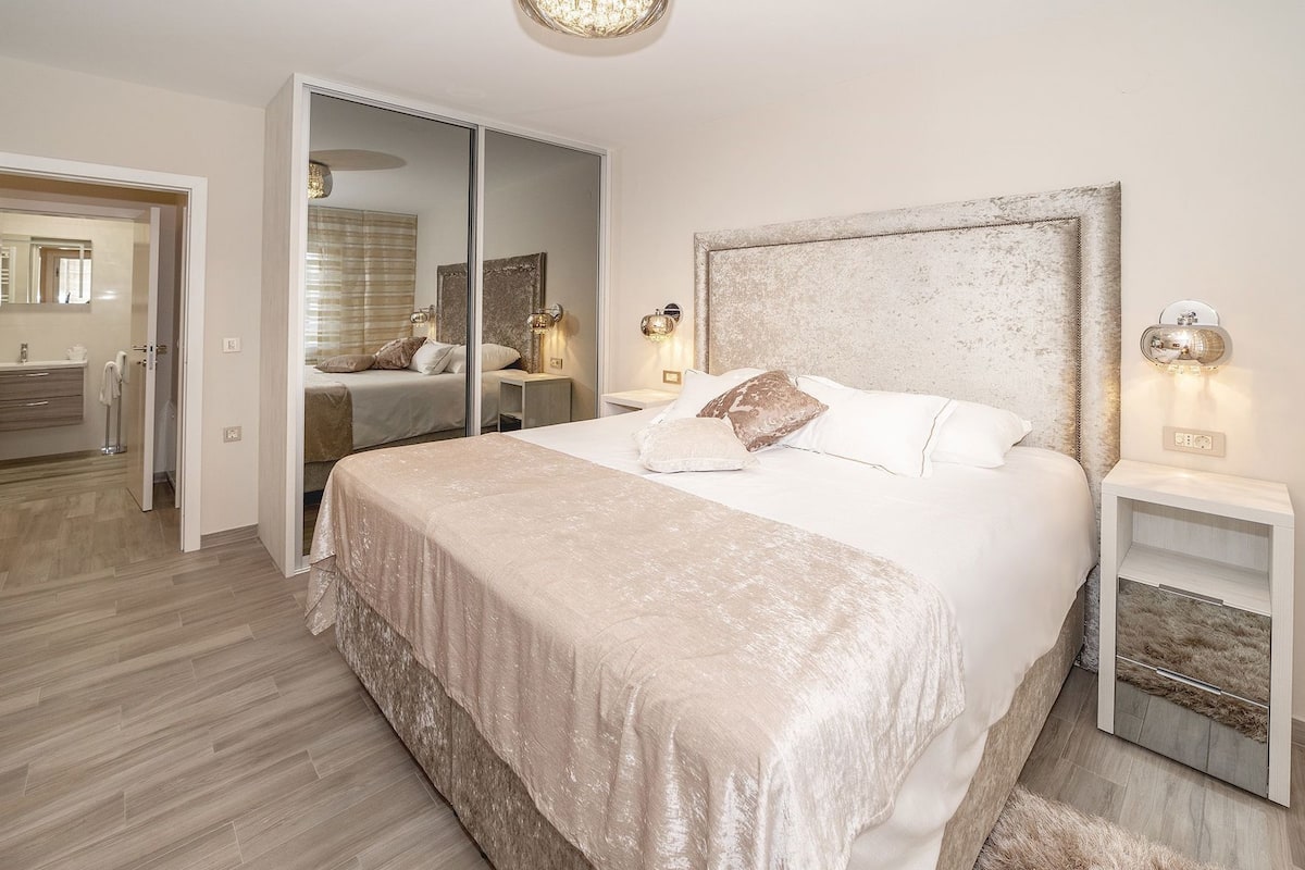 Een slaapkamer met een groot bed, een spiegel, nachtkastjes en een garderobe.