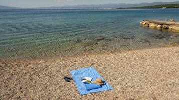 A clear lake with a rocky shore, a blue towel with items on it, and a distant mountain range.