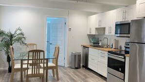 Uma cozinha moderna com armários brancos, eletrodomésticos de aço inoxidável e um espaço de jantar com cadeiras de madeira e uma mesa de vidro.