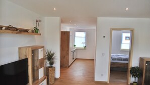 A spacious living area with a wooden floor, a flat-screen TV, and a large window providing natural light. - Ferienwohnung STADTOASE Apartmenthaus (Frankenberg)