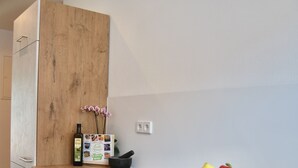 A modern kitchen with a wooden cabinet, a stainless steel bowl of fruit, a bottle, and a small potted orchid. - Ferienwohnung STADTOASE Apartmenthaus (Frankenberg)