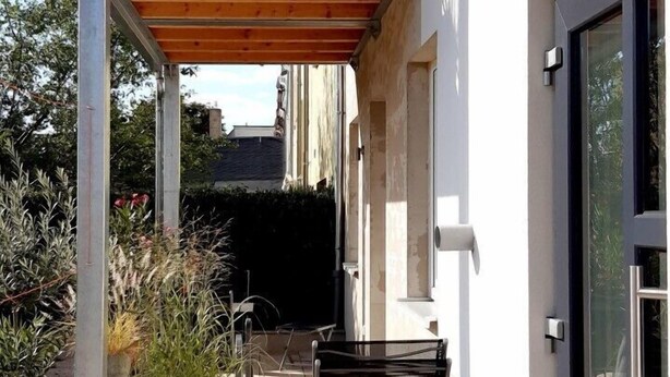A covered outdoor area with a wooden bench, potted plants, and a metal railing. - Ferienwohnung STADTOASE Apartmenthaus (Frankenberg)