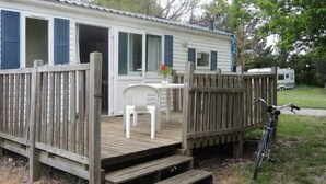 A mobile home with a wooden deck, a single chair, and a bicycle parked outside.