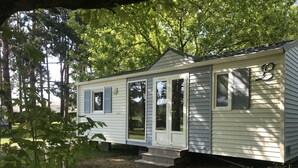 A small, single-story mobile home with a front porch, a sliding glass door, and a small attached garage.