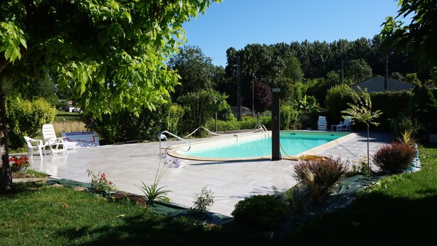 A swimming pool with a tiled deck, surrounded by greenery and a few lounge chairs.