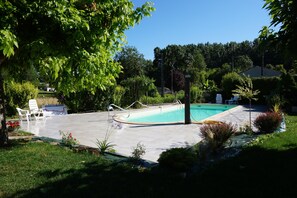 Ein Schwimmbecken mit gefliestem Sonnendeck, umgeben von Grünpflanzen und einigen Liegestühlen.