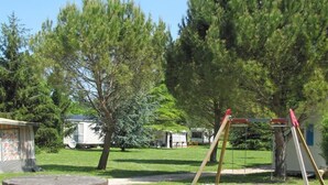 A grassy outdoor area with a swing set, a stone bench, and a small shed.