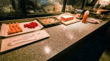 A buffet counter with various food items including sliced carrots, cherry tomatoes, and a dish with shrimp.