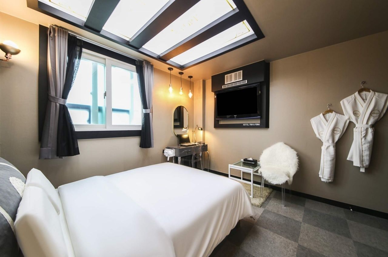 Una habitación de hotel con cama, escritorio con espejo, televisión y ventana con cortinas.