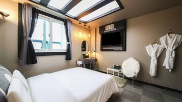 Una habitación de hotel con cama, escritorio con espejo, televisión y ventana con cortinas.